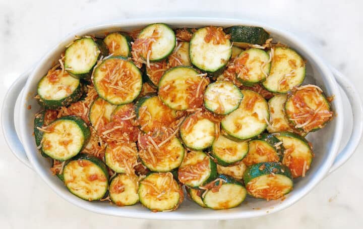Transferring the coated zucchini to the baking dish.