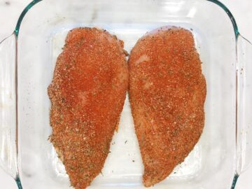 Two Cajun-spiced chicken breasts in a baking dish, before baking.