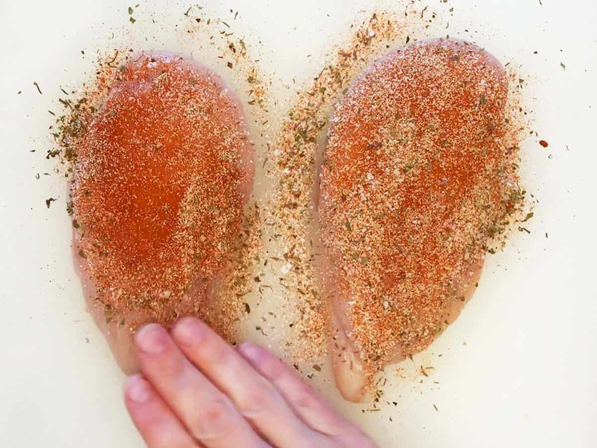 Seasoning chicken breasts with Cajun spices.