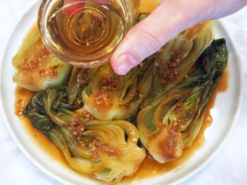Topping the cooked bok choy with sesame oil.