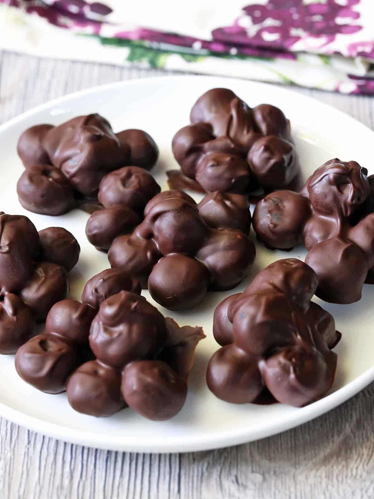 Chocolate covered blueberries are served on a white plate with a napkin.