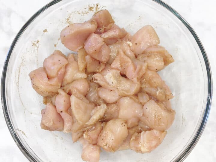 Coating the chicken pieces in marinade before grilling them.