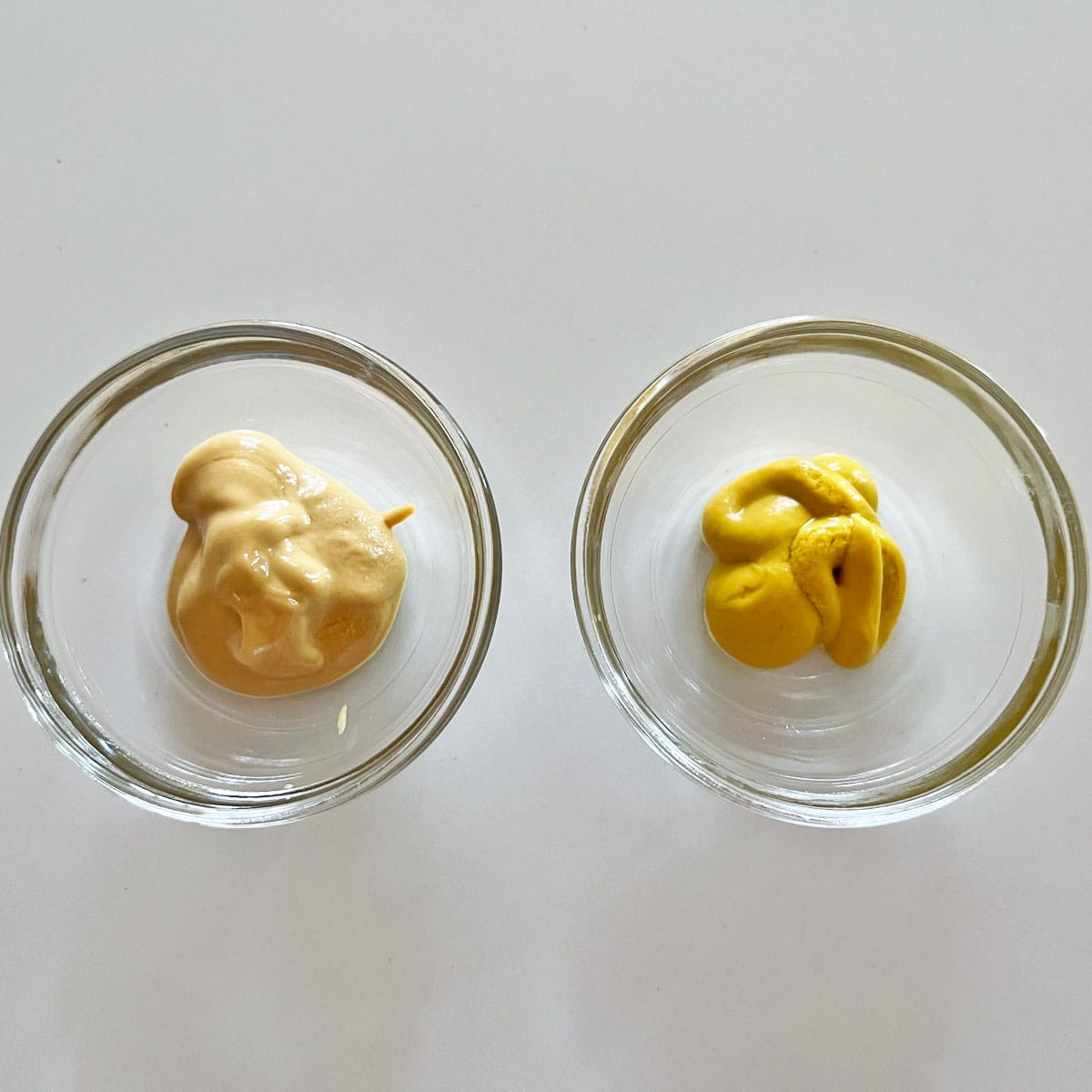 A small bowl with Dijon mustard and another with yellow mustard.