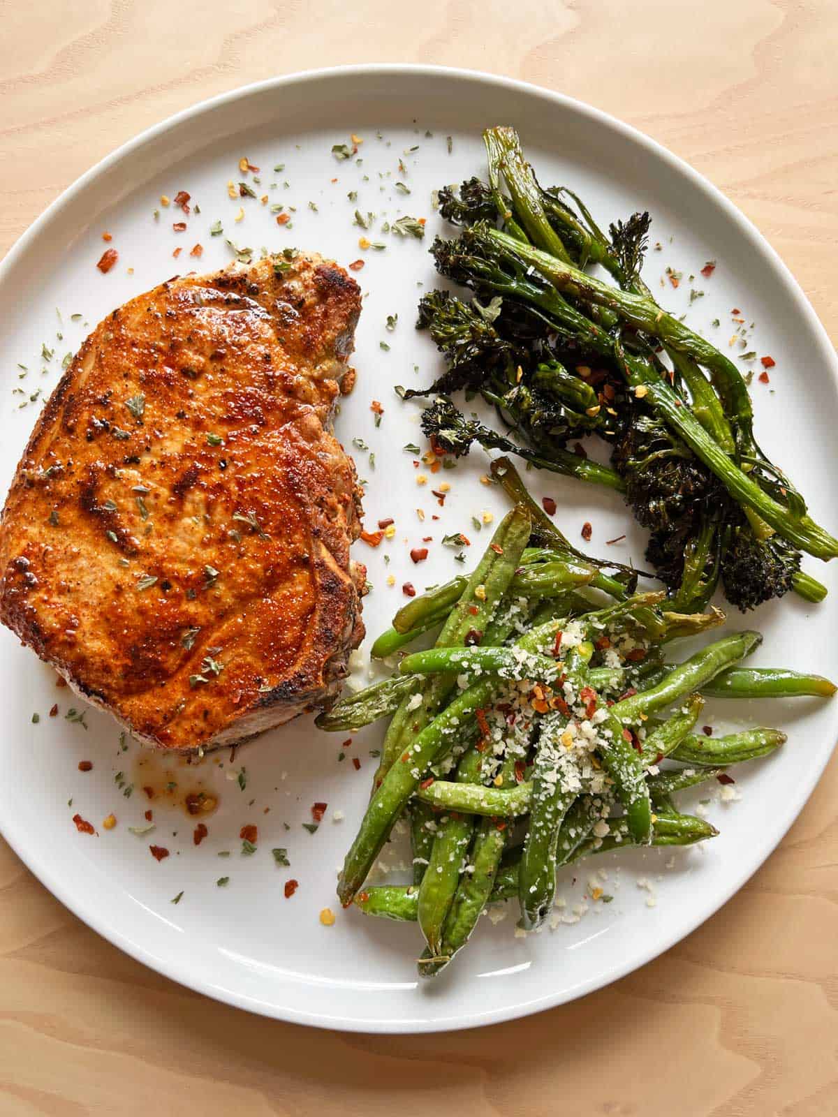 A baked pork chop is served with green beans and broccolini.