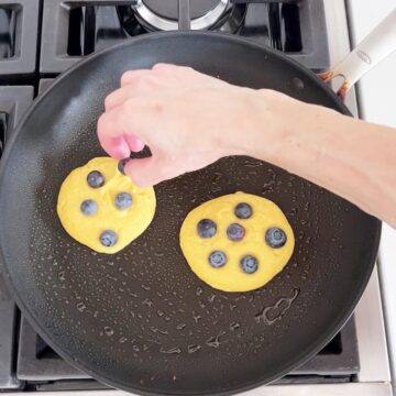 Topping the pancakes with blueberries in the skillet.