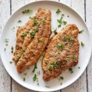 Two baked catfish fillets are served on a white plate.