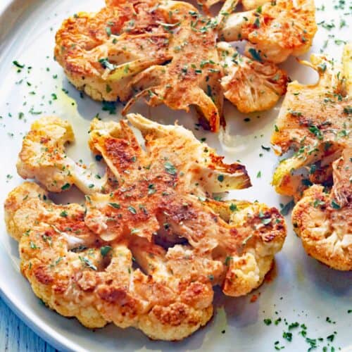 Three cauliflower steaks are served on a white plate.