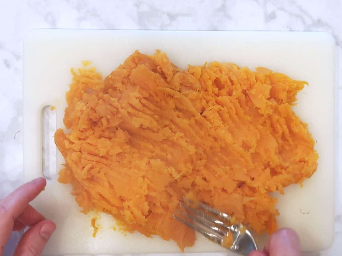Mashing the sweet potato on the cutting board.