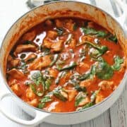 A pork stew is served in a white saucepan with a napkin.