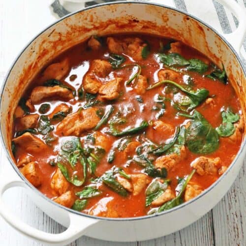 A pork stew is served in a white saucepan with a napkin.