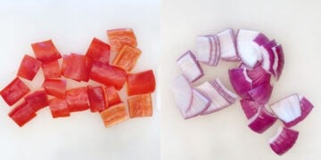 Peppers and onions are chopped on a cutting board.