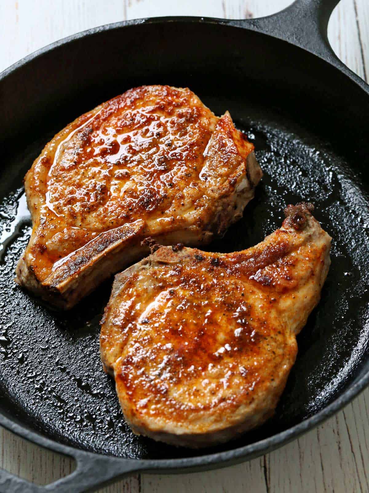 Two pork chops in a cast-iron skillet.