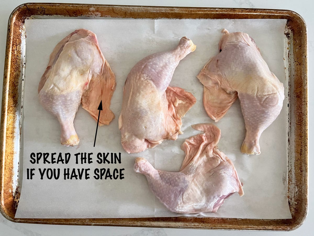 Four chicken leg quarters in a pan. The skin was spread on the pan to help it become crispy.