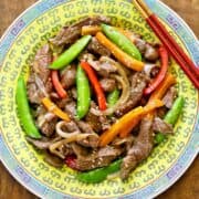 A steak stir fry is served on a yellow Chinese plate with red chopsticks.