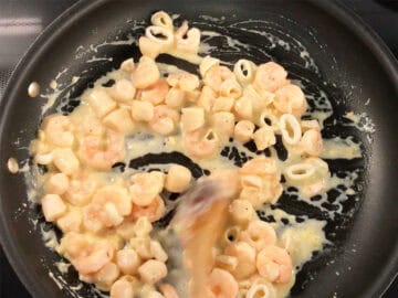 Adding back the seafood to the skillet and mixing it with the sauce.