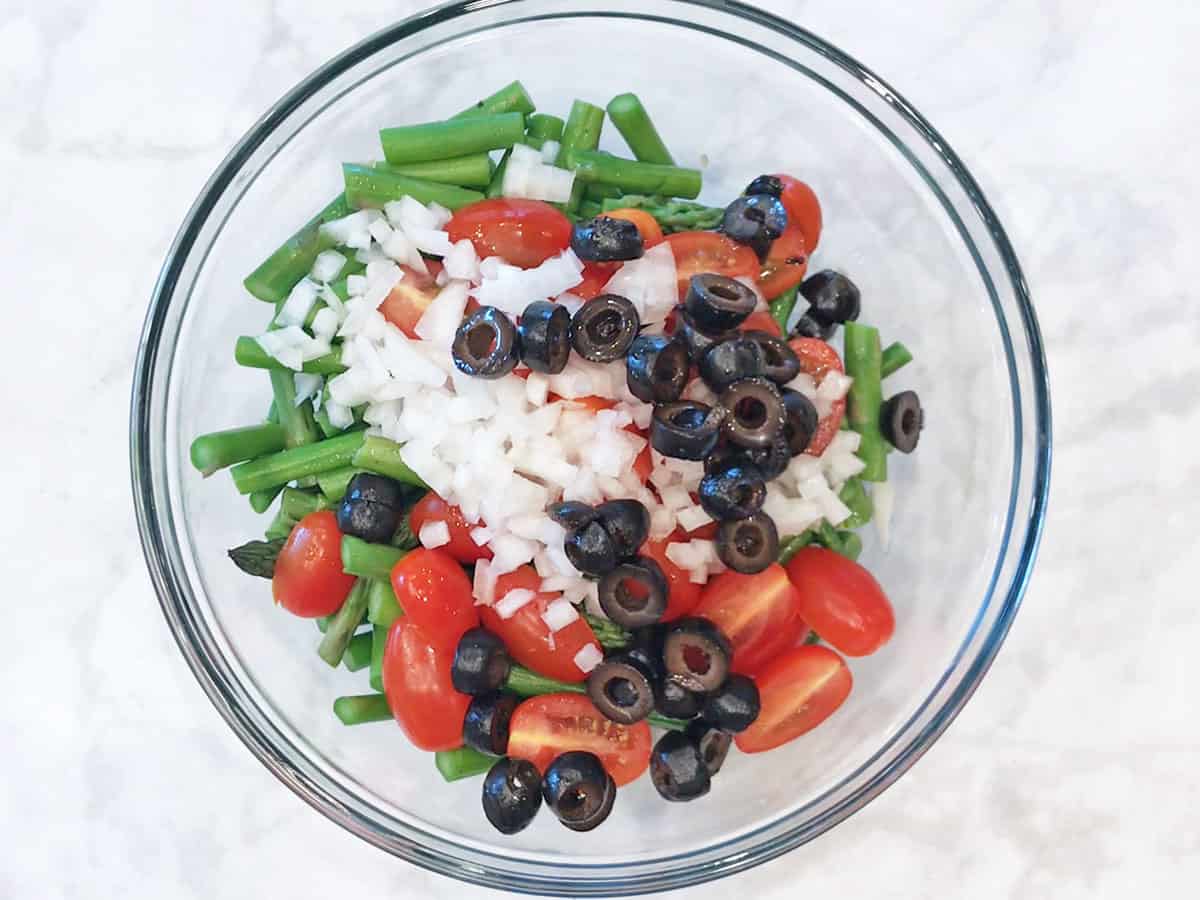 Asparagus, tomatoes, onions and olives in a bowl.