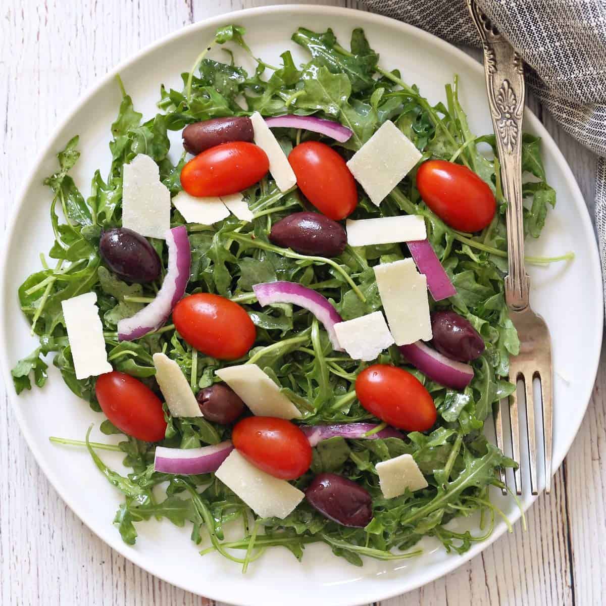Arugula salad is served on a white plate.