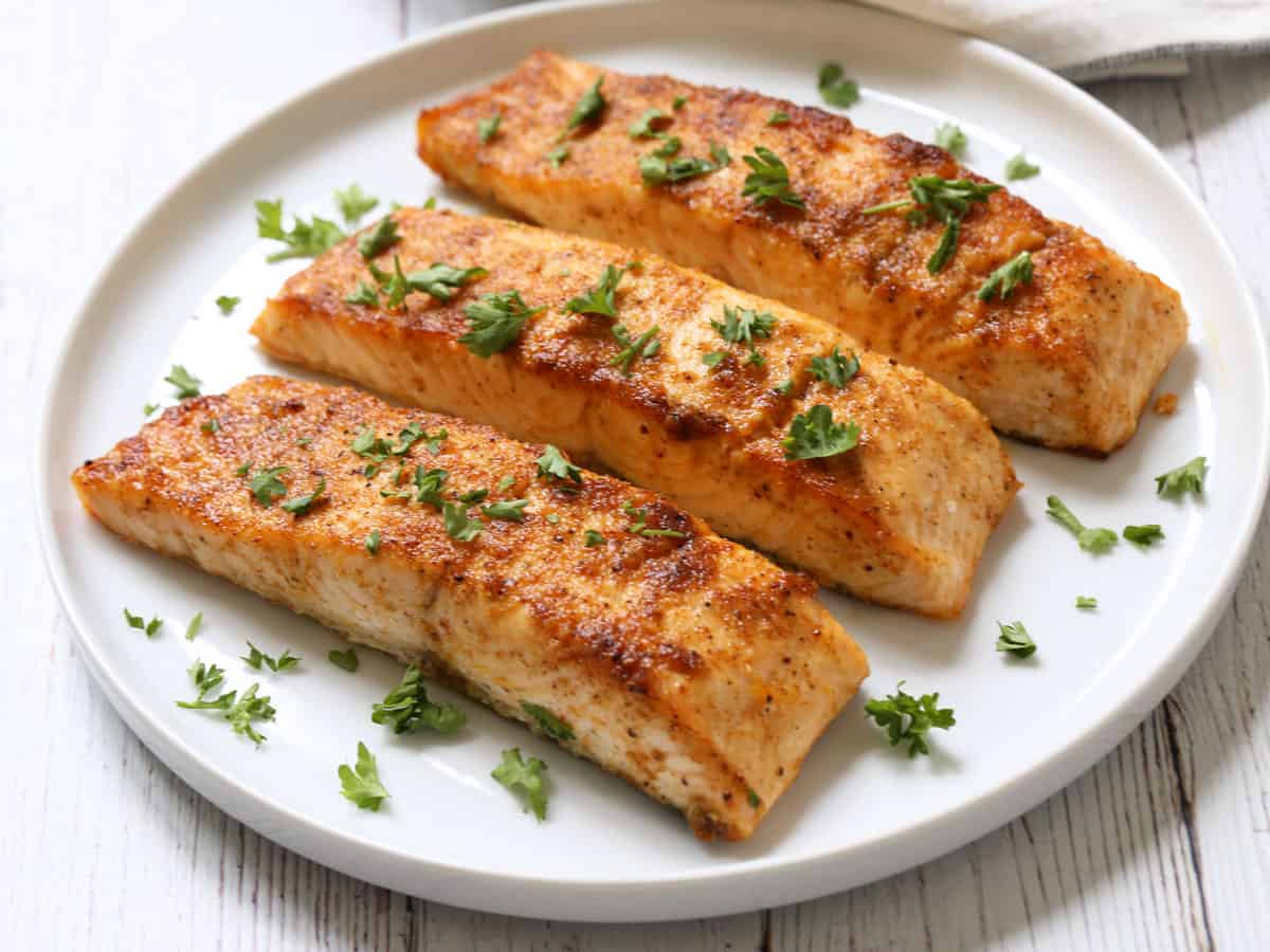 Three broiled salmon fillets are served on a white plate.