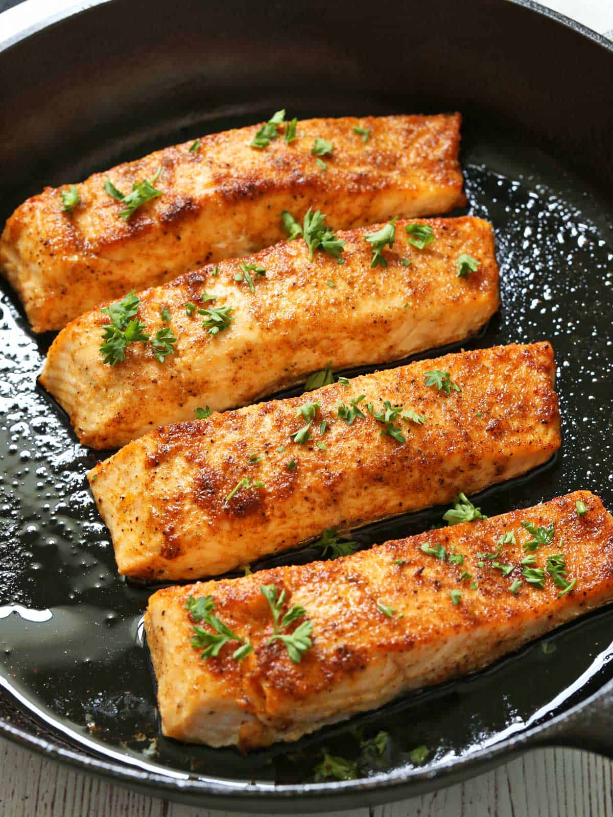 Four pieces of broiled salmon in a cast-iron skillet.