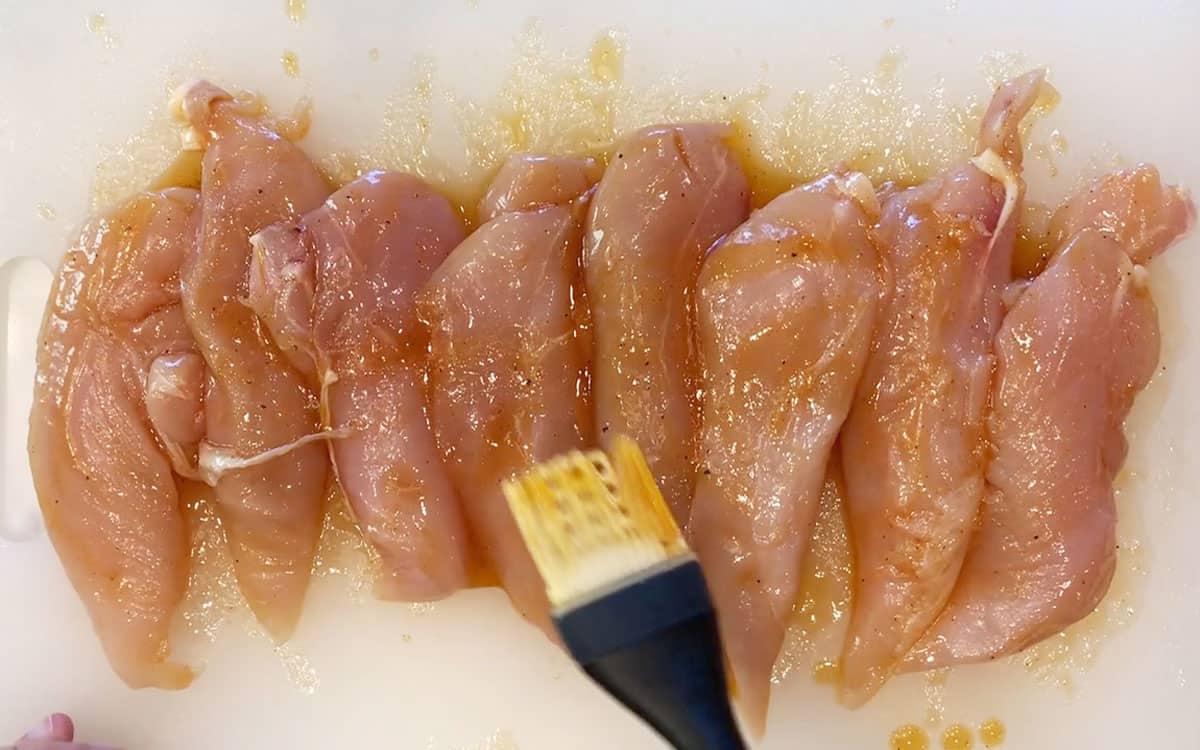 Brushing the chicken tenders with the marinade.