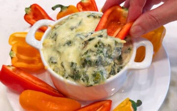 Spinach artichoke dip is served with mini peppers.