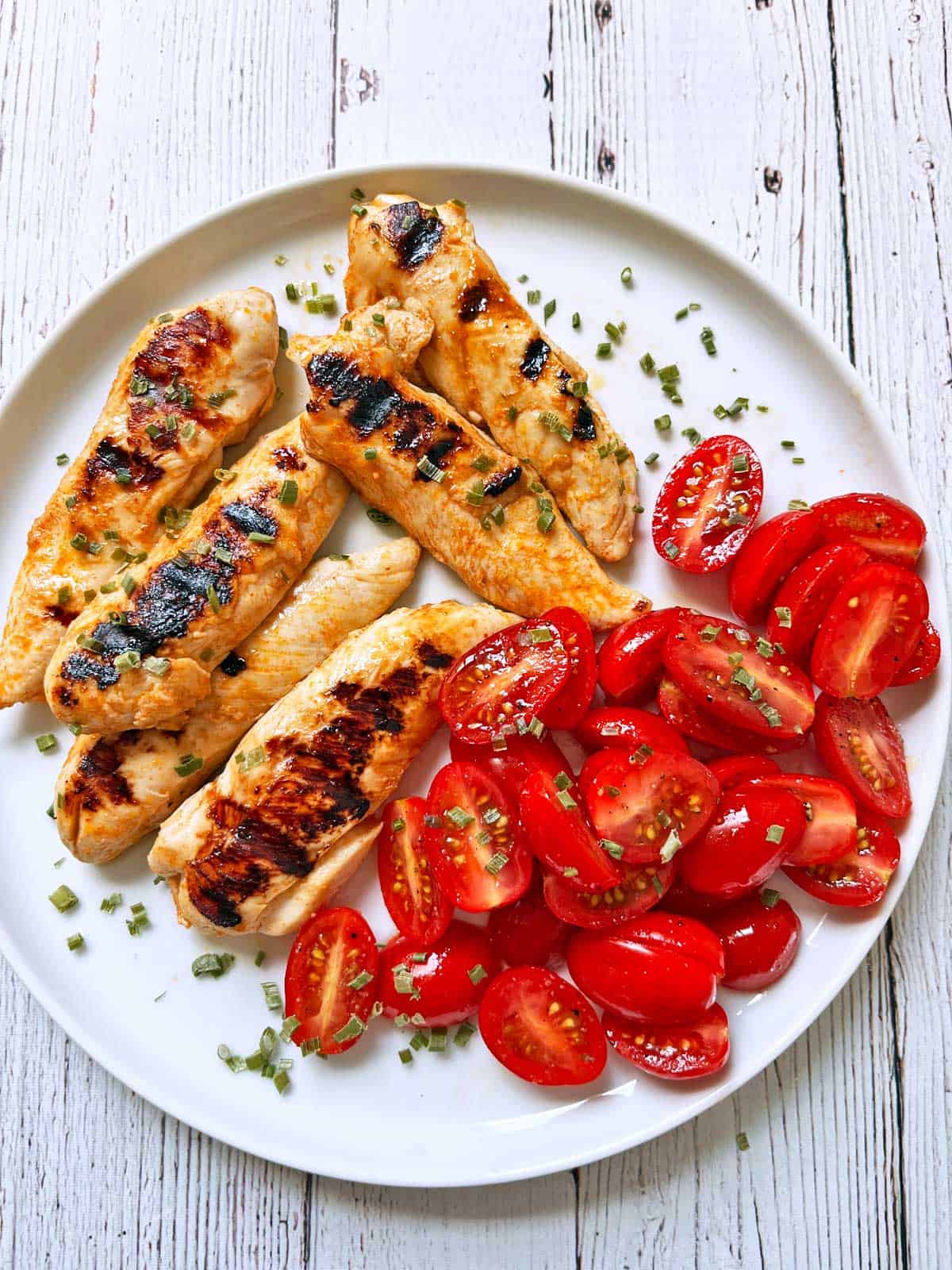 Grilled chicken tenders are served with a tomato salad.