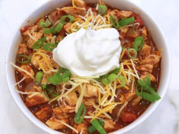 Leftover turkey chili is served in a bowl, topped with scallions, shredded cheese, and sour cream.
