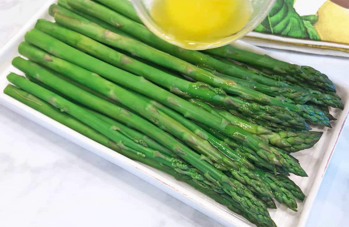 Drizzling the steamed asparagus with melted butter.