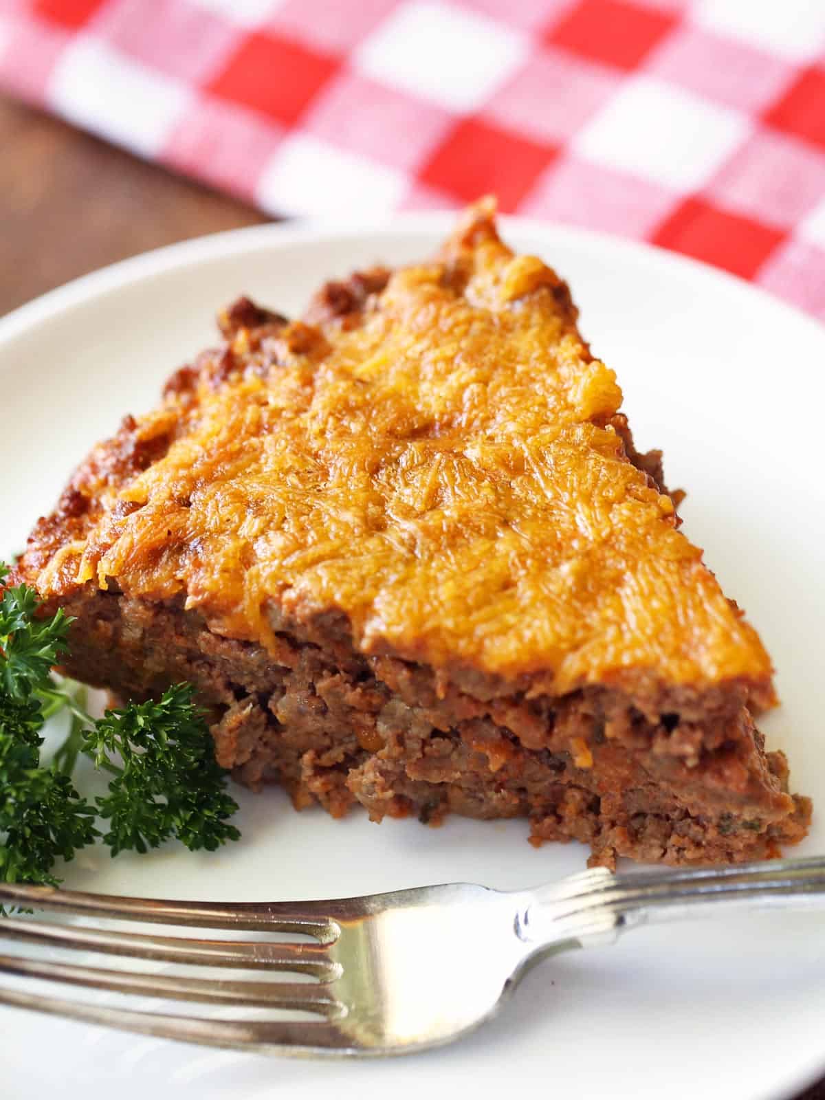 A slice of keto meat pie is served on a white plate with a fork.