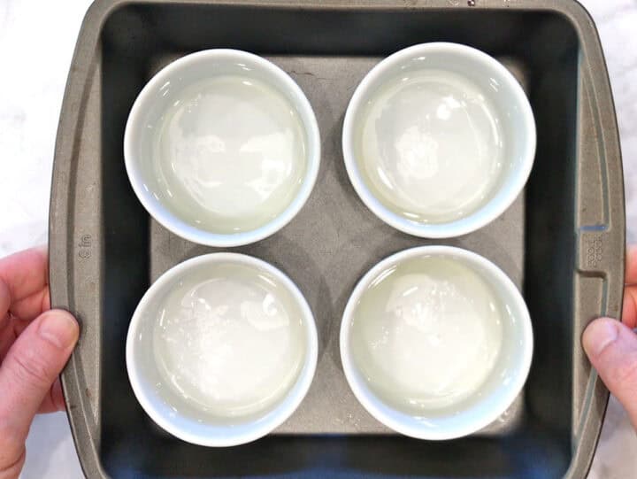 Four greased ramekins in a rimmed baking dish.