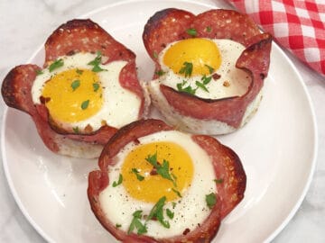 Salami and egg cups are served on a white plate.