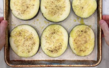 Oiled and seasoned eggplant slices on a baking sheet.