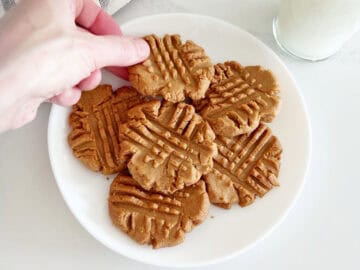 A hand picking up a peanut butter cookie from a plate.