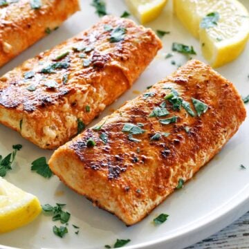 Grilled mahi mahi is served on a white plate with lemon slices.