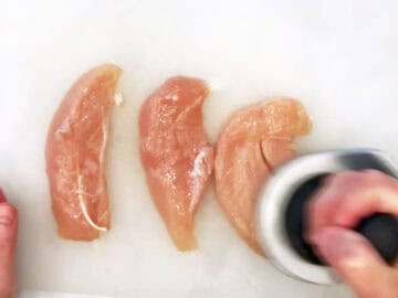 Pounding the chicken with a meat pounder.