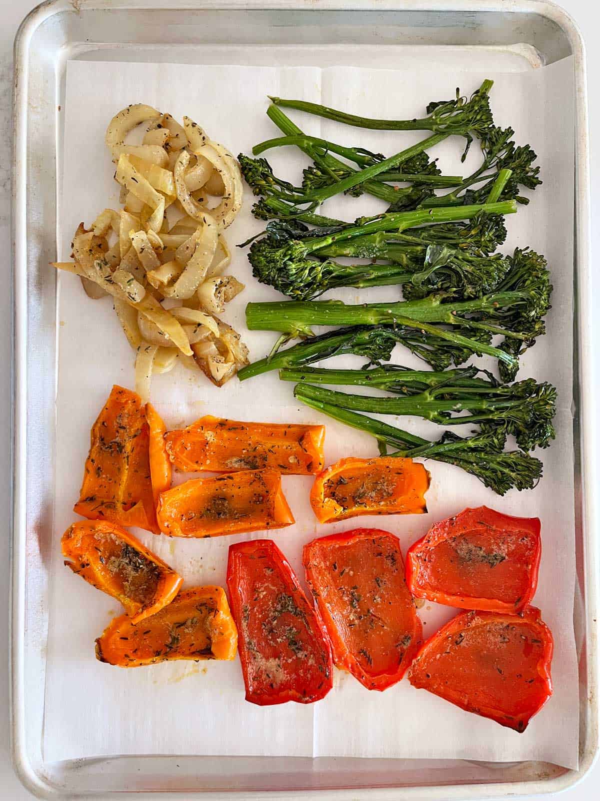 A sheet pan with roasted broccolini, peppers, and onions.