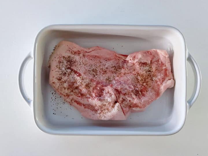 A seasoned pork jowl in a white baking dish.
