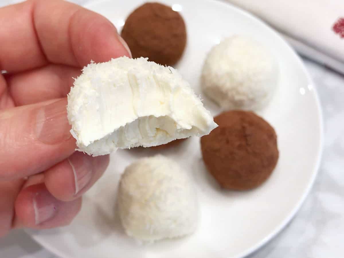 A hand is holding a bitten cheesecake bite.