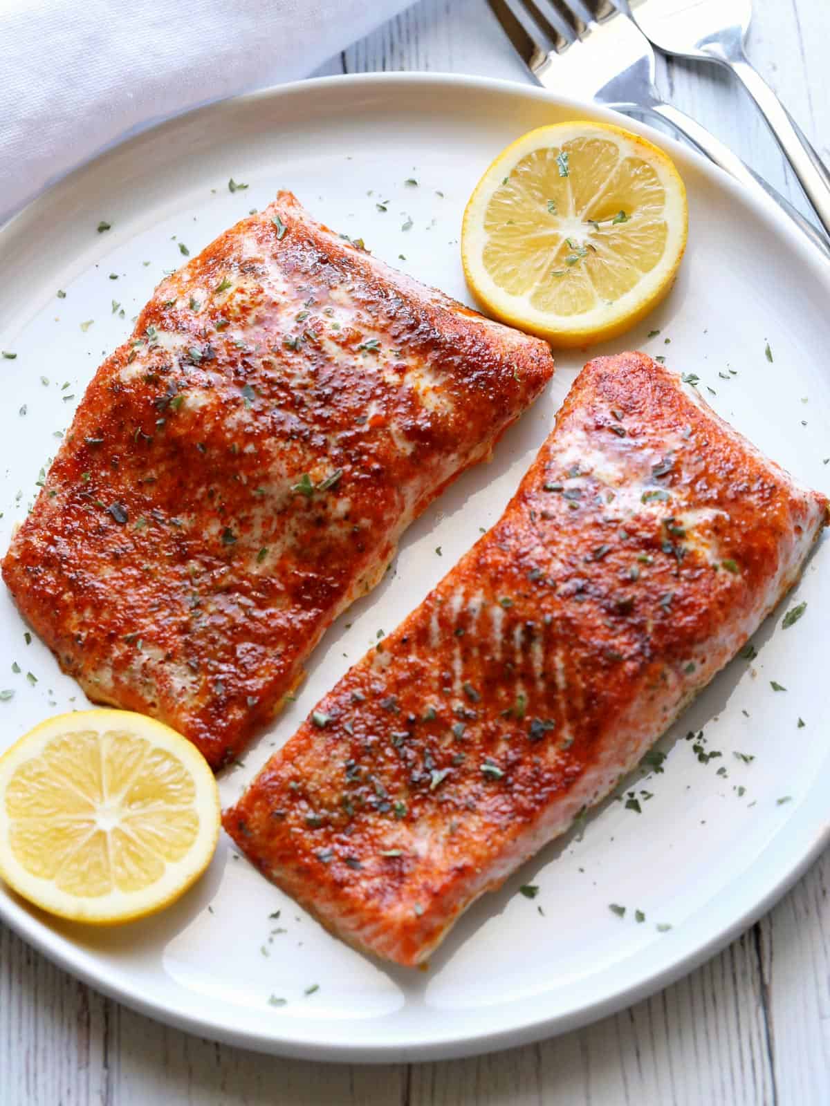 Paprika salmon is served on a white plate with a slice of lemon for garnish.