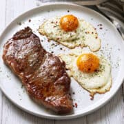 Steak and eggs are served on a white plate.