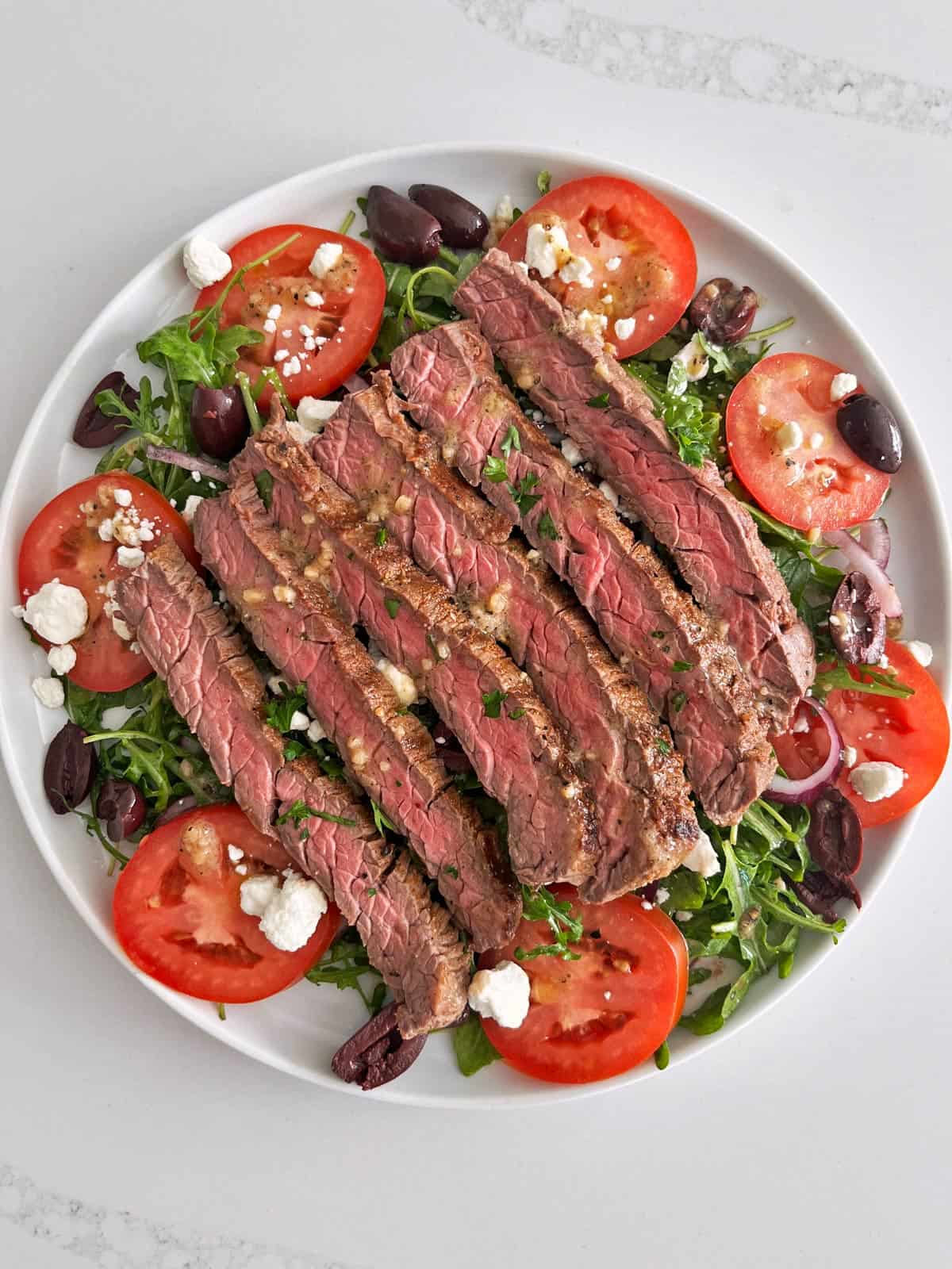A steak salad is served on a white plate.