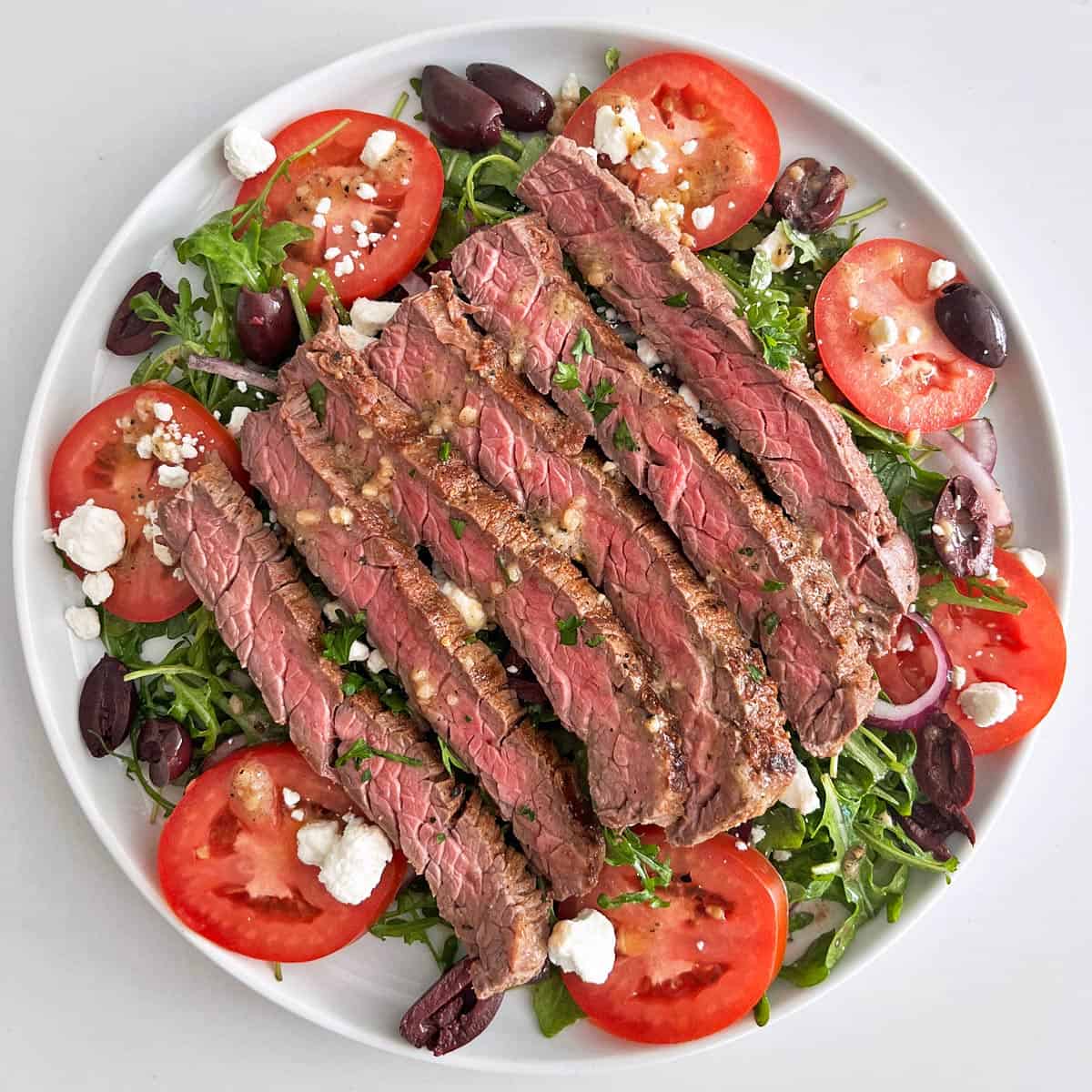 A steak salad is served on a white plate.