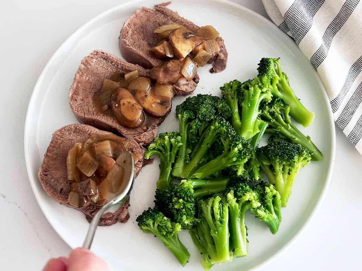 Topping tongue slices with the sauce. They are served on a plate with broccoli.