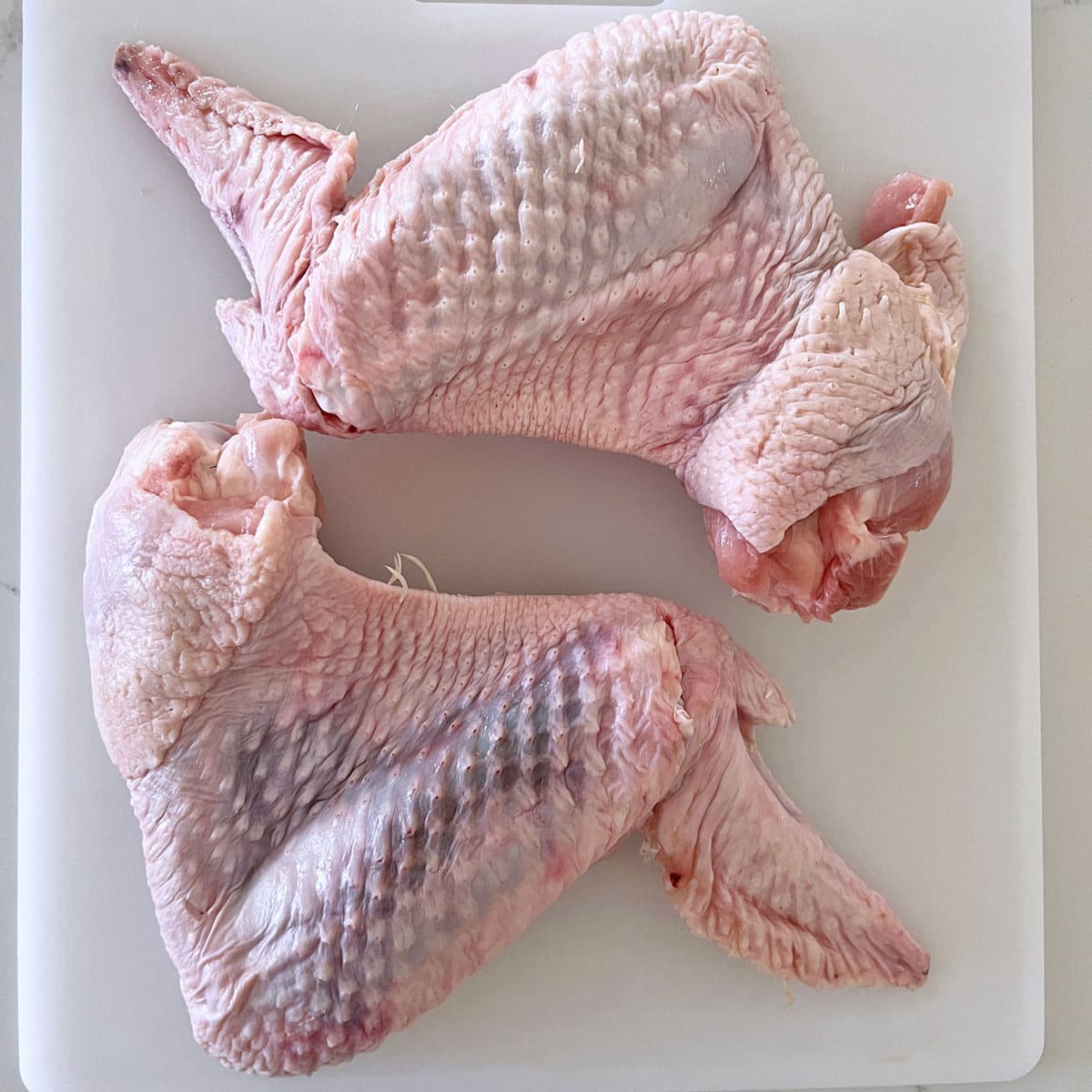Two large turkey wings on a cutting board.