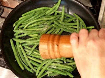 Adding the green beans, salt, and pepper to the skillet.