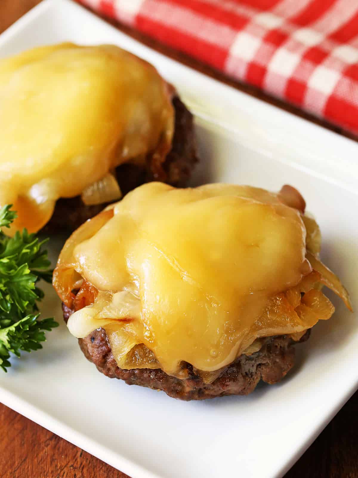 Two broiled burgers are served on a white plate.