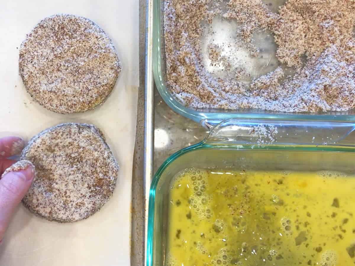 Eggplant slices were coated in almond meal and placed on a white cutting board.
