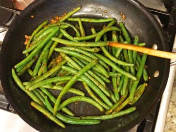 Cooking the green beans with hot sauce, garlic, and honey.