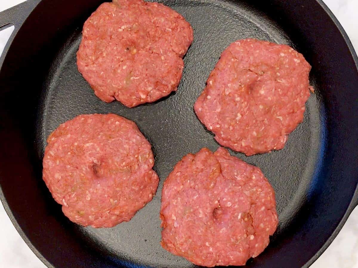 Four dimpled burgers in a skillet.