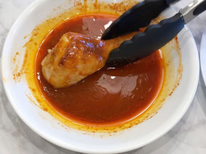 Dipping a drumstick in buffalo sauce.